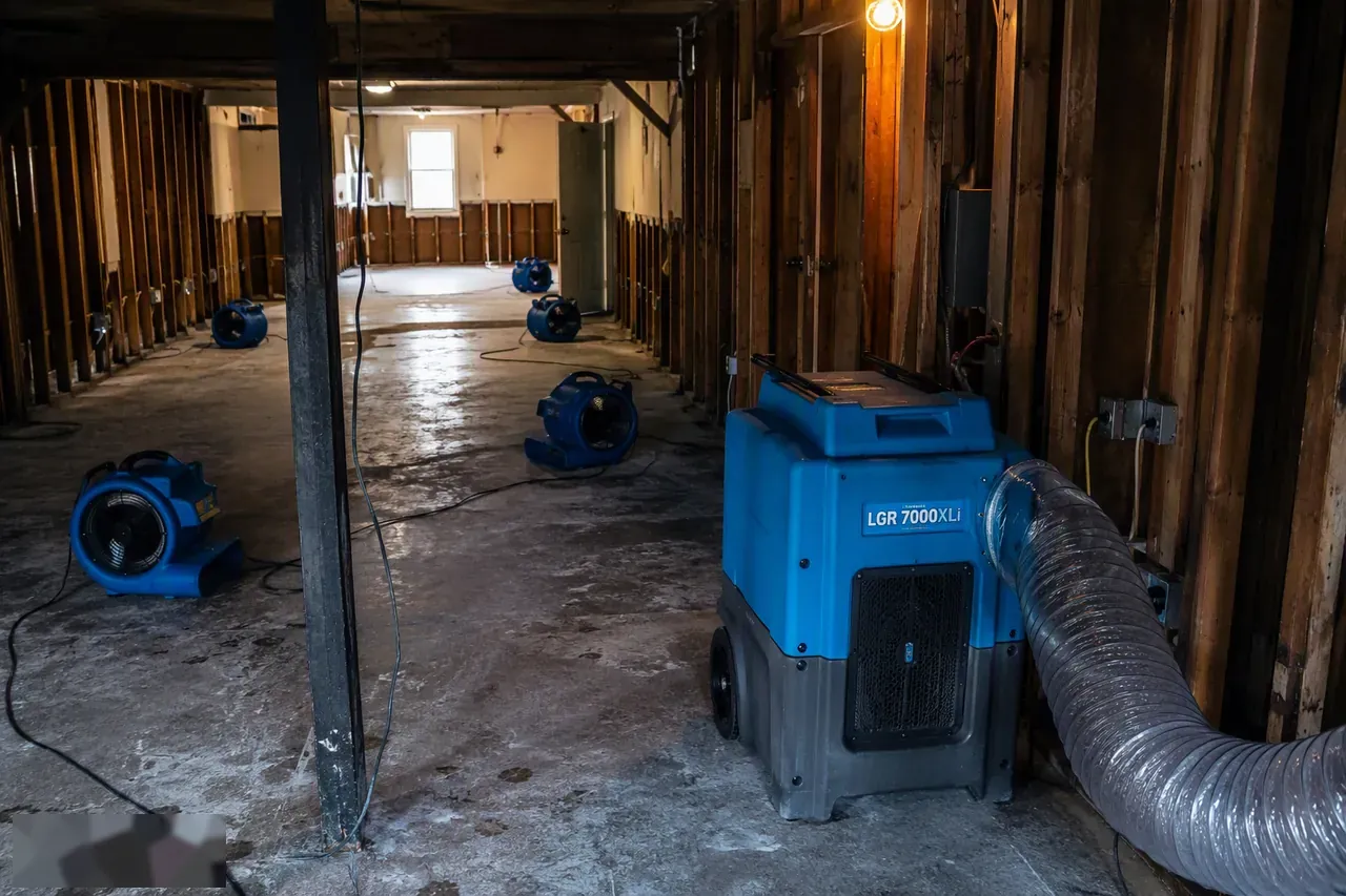 Commercial air movers and dehumidifier drying a flood-damaged room with exposed framing